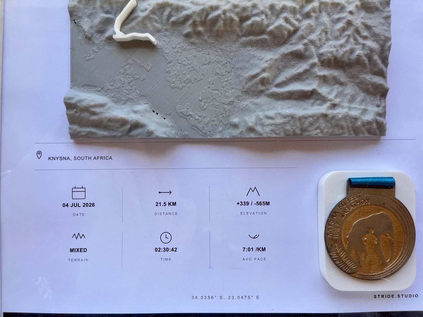 Flat lay of a 3D printed topographic route relief beside the printed race stats panel